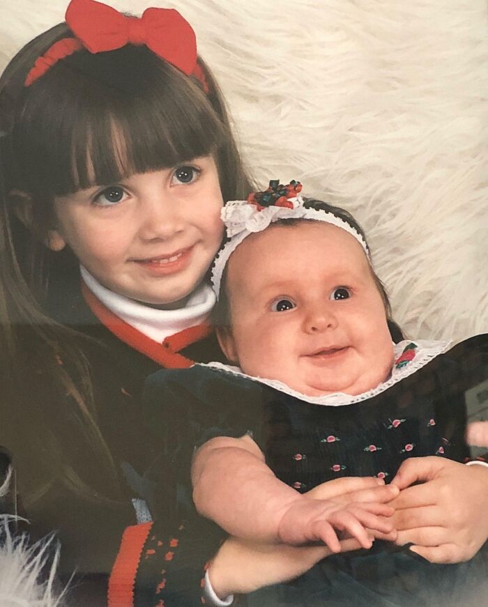 Two young girls in matching outfits smiling awkwardly in a hilariously awkward childhood photo with a playful vibe.