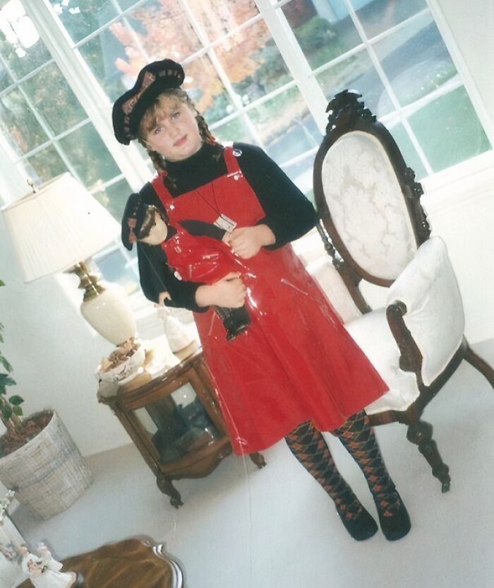 Young girl in a red dress and patterned tights holding a toy stick in a hilariously awkward childhood photo.