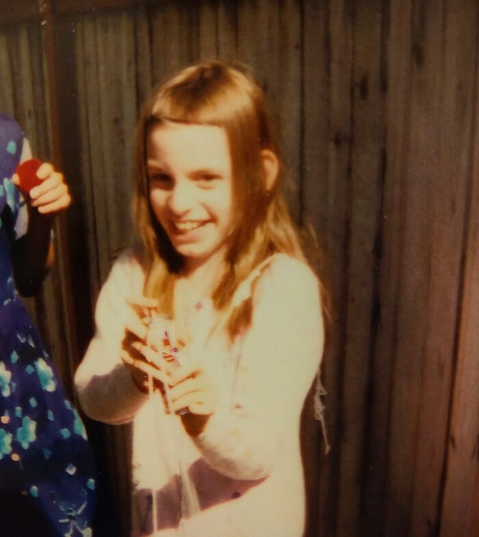 Young girl smiling awkwardly while holding a toy, one of the hilariously awkward childhood photos from the collection.