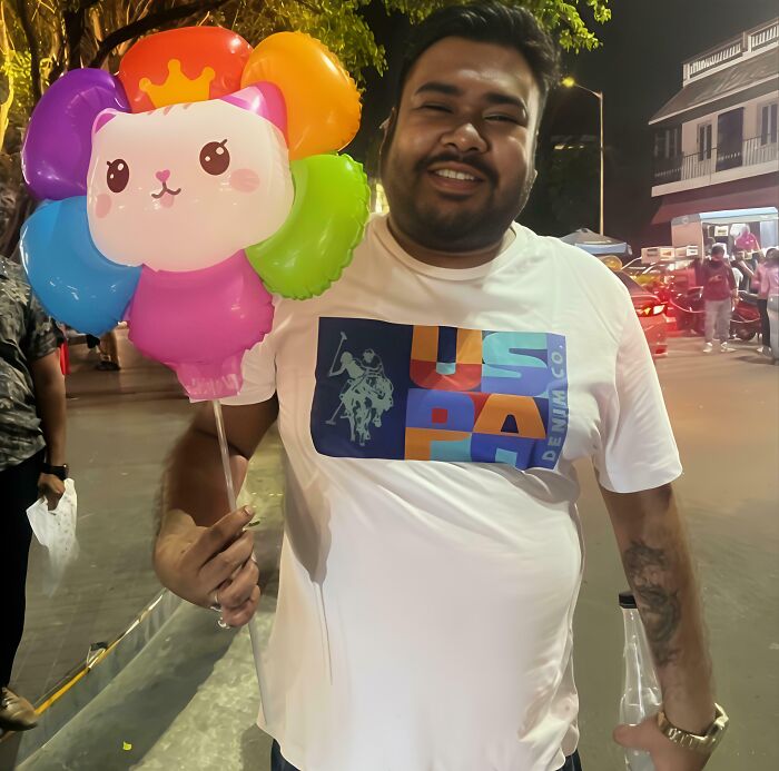 Man smiling at night market holding colorful cat-shaped balloon, capturing leap of faith moments and best life decisions.