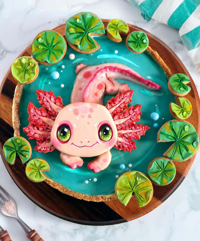 Masterfully crafted cake shaped like a colorful axolotl with lily pads on a blue water-like surface.