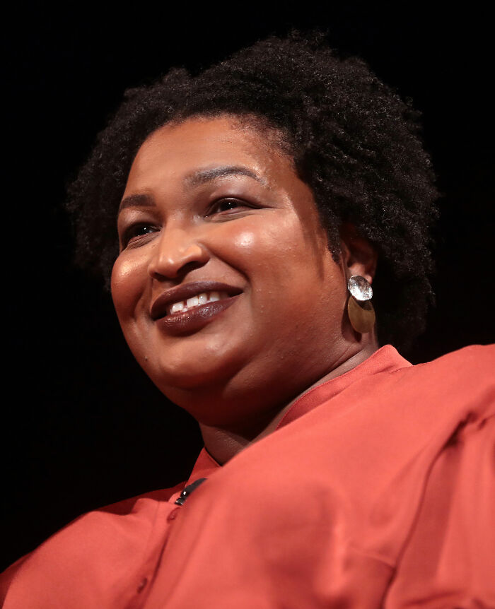 Stacey Abrams smiling in a close-up portrait, wearing earrings and a red top during a public speaking event.