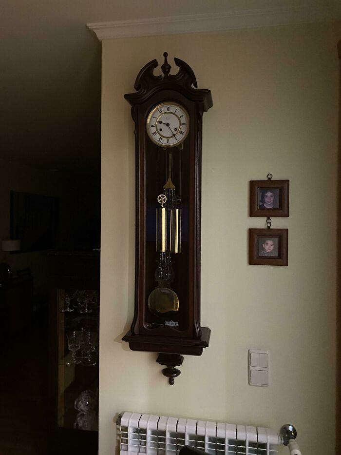 Antique wooden wall clock with pendulum and framed photos in a cozy room, inspired by Stranger Things memes.