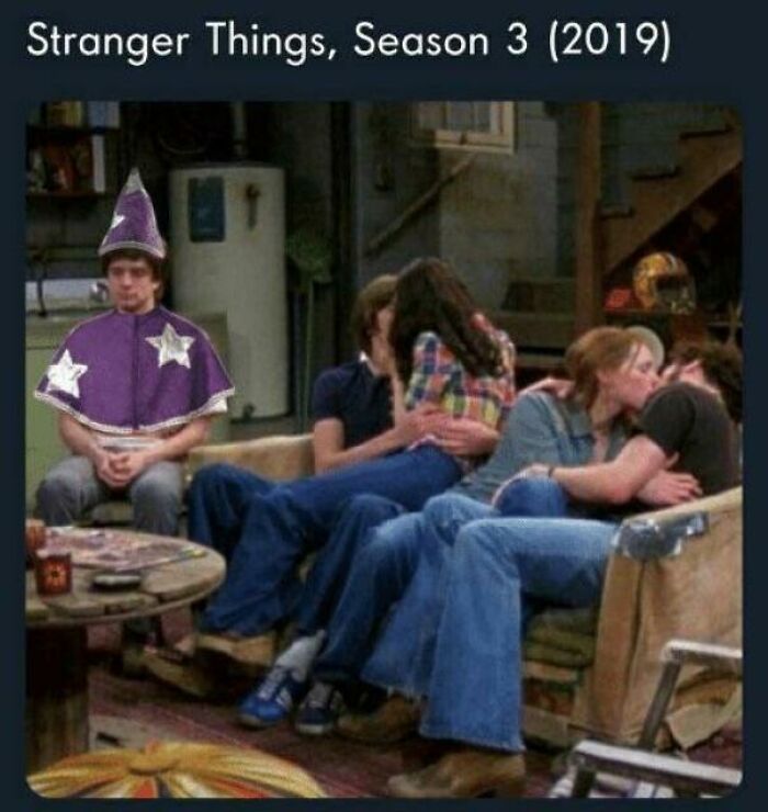Man dressed as wizard sitting alone while couples cuddle on a couch, a funny Stranger Things meme about feeling left out.