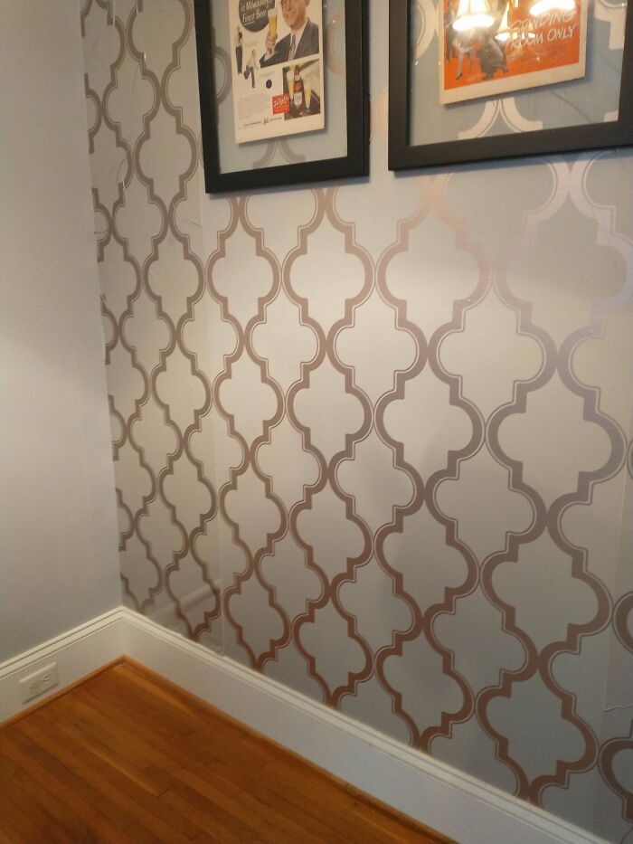 Patterned wallpaper corner with hardwood floor and framed pictures in a room showing decor details and snobbish style.