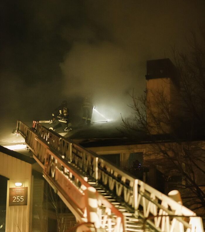 Firefighters on a ladder extinguishing a rooftop fire, showcasing one of the fascinating jobs that make a 9-to-5 more bearable.