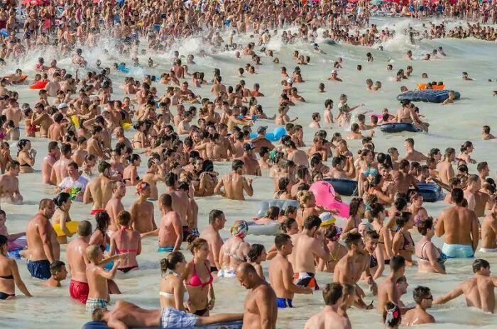 Large crowd of people gathered in shallow water under sunlight, illustrating challenges in solving weird math problems.