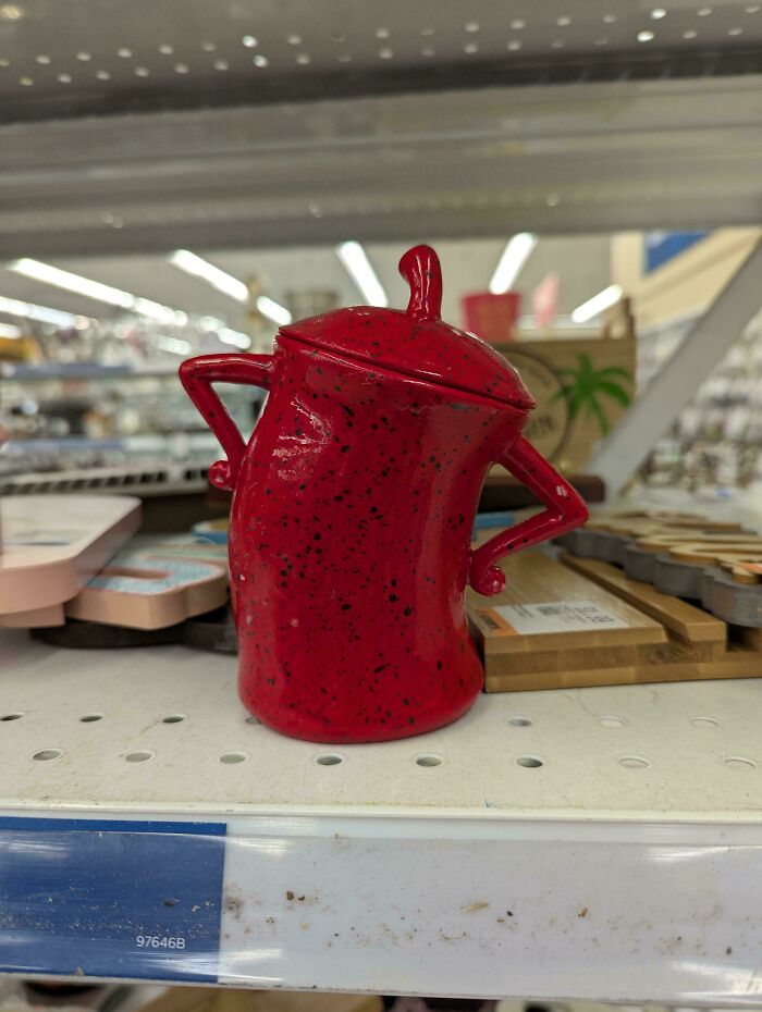Red speckled ceramic teapot with arms on hips on a store shelf showing cool secondhand store surprise.