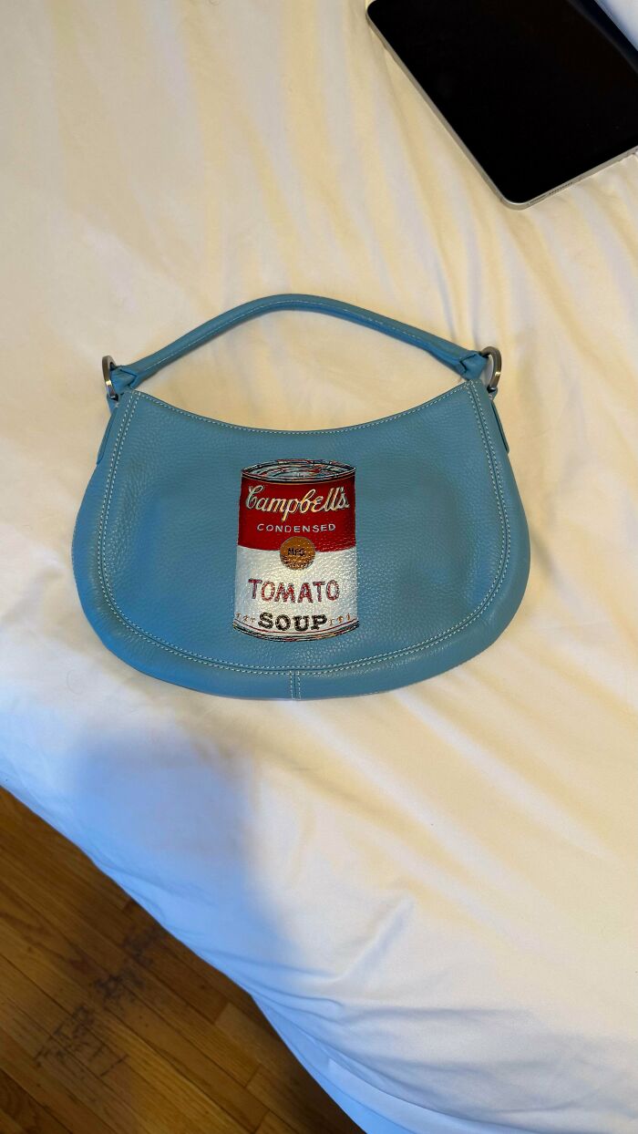 Blue handbag with Campbell's Tomato Soup design laying on a white sheet, an example of secondhand stores cool surprises.