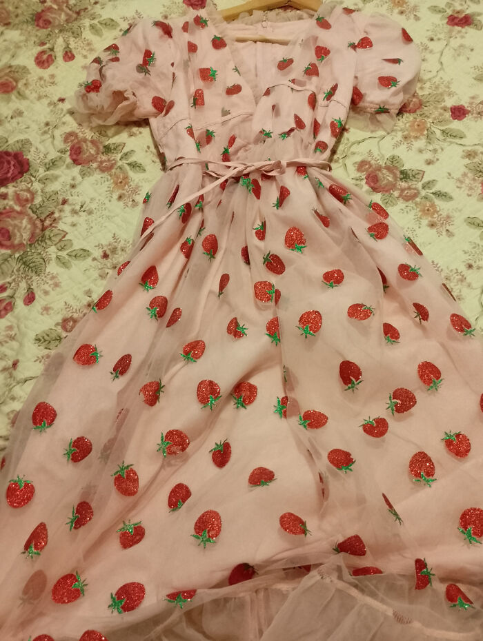 Pink dress with strawberry patterns laid out on a floral secondhand store bed, showcasing cool unexpected surprises.
