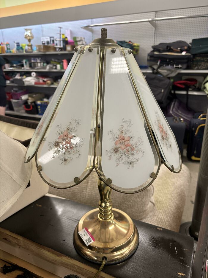 Vintage floral table lamp found at a secondhand store with brass base and decorative glass panels in a thrift shop setting.