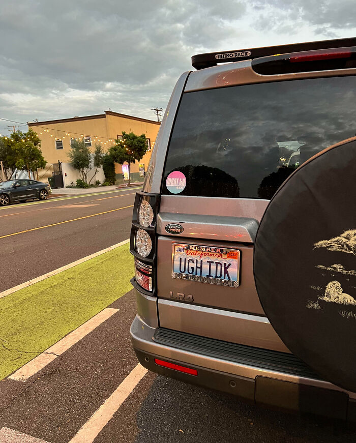 Personalized license plate reading UGH IDK on a Land Rover parked on a city street during cloudy evening.