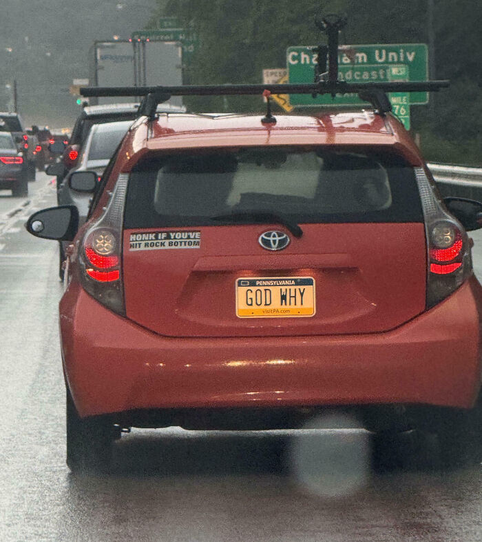 Red Toyota car with a personalized license plate reading GOD WHY, a humorous example of personalized license plates on a rainy day.
