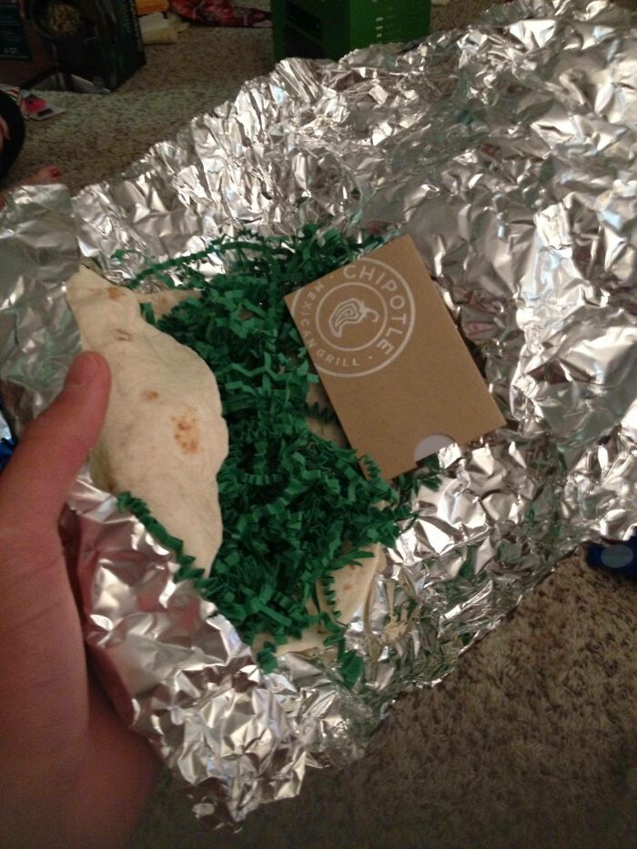 Hand holding a funny gift wrap designed like a Chipotle burrito with foil and green paper, inspiring Christmas mischief.