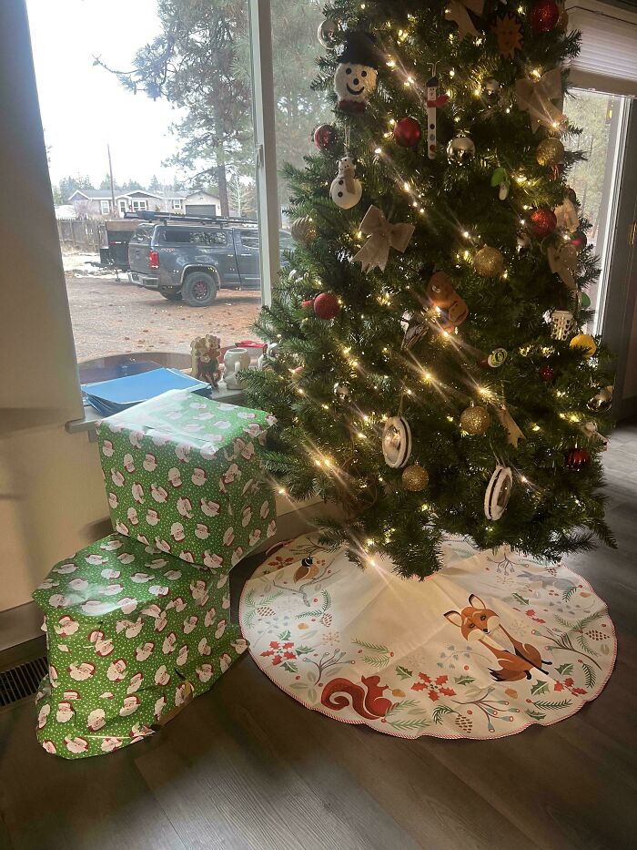 Christmas tree decorated with lights and ornaments next to gifts wrapped in funny gift wraps with Santa patterns.