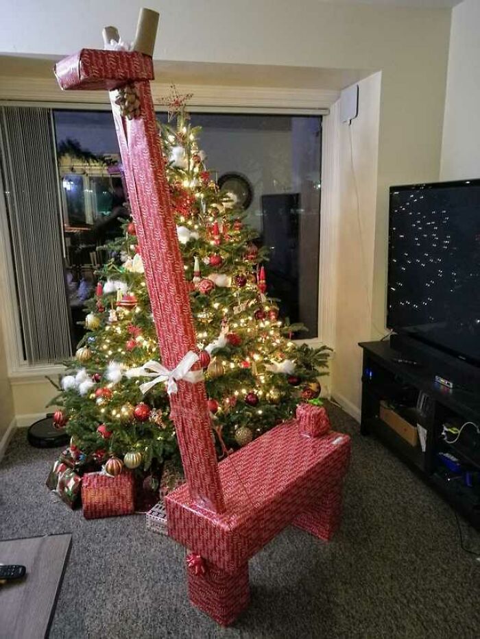 Giraffe-shaped gift creatively wrapped in red patterned paper beside a decorated Christmas tree, showcasing funny gift wraps.