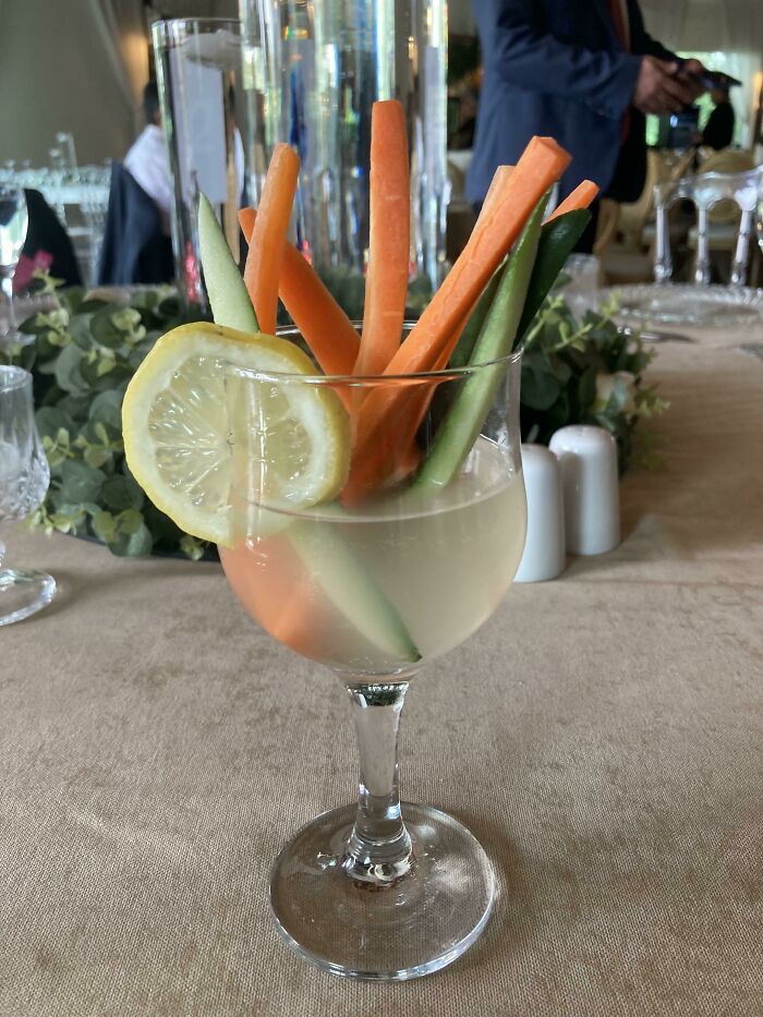 Glass with lemon slice holding carrot and cucumber sticks in a dining setting, an outrageous meal that looks nothing like menu photos.