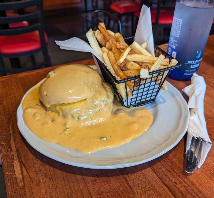 Burger smothered in thick sauce with fries in a basket on a plate, part of outrageous meals that look nothing like menu photos.