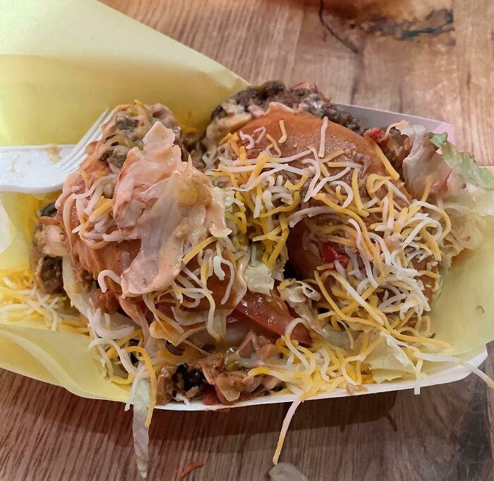 Messy cheeseburger with shredded cheese and sauce failing to match menu photo expectations of outrageous meals.