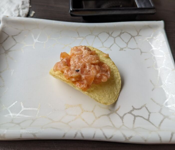 Small portion of seafood topping on a single chip, an example of outrageous meals that look nothing like menu photos.