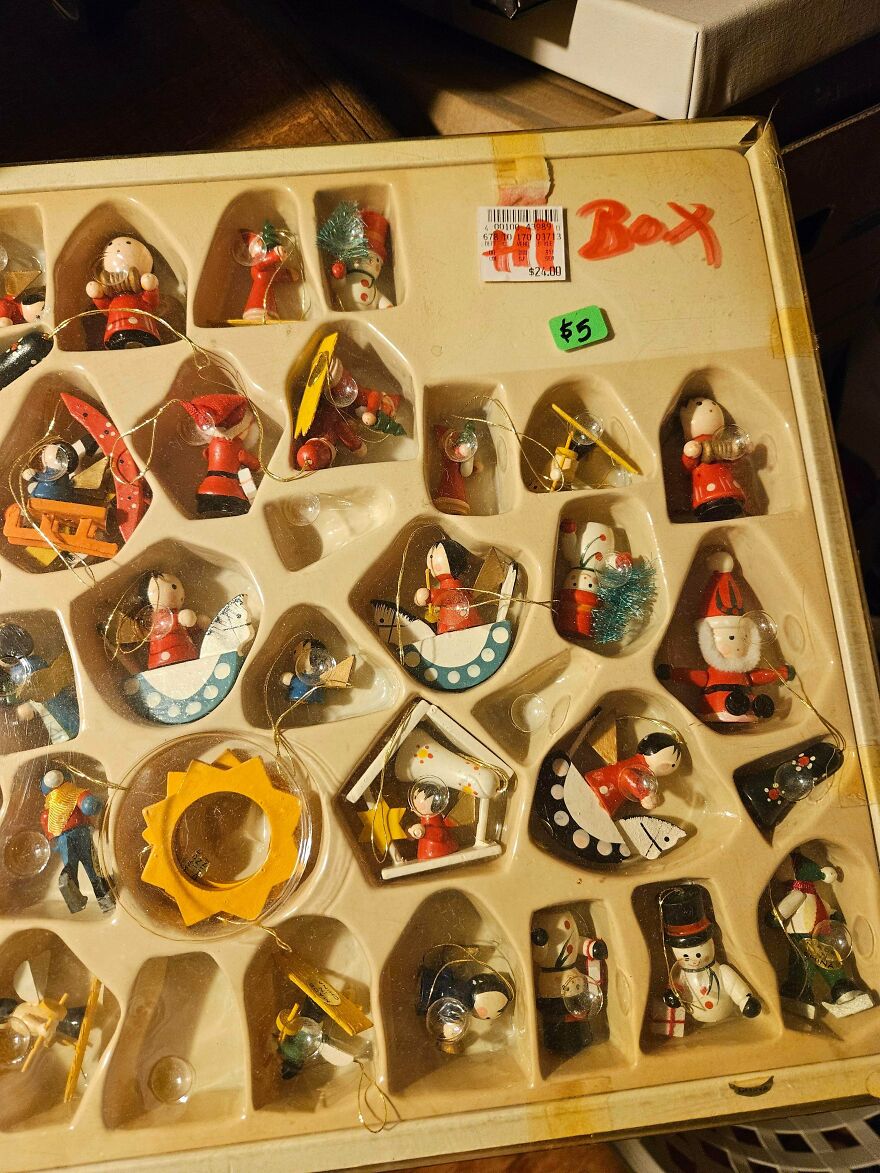 Box of nostalgic vintage Christmas decorations including small painted wooden ornaments in various festive shapes and characters.