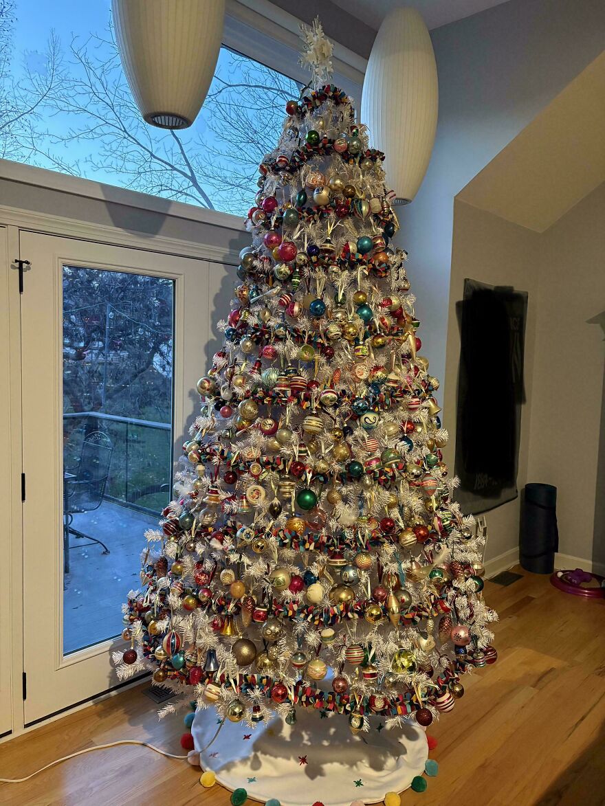 Vintage Christmas decorations on a white tree with colorful ornaments and nostalgic holiday charm in a cozy living room setting.