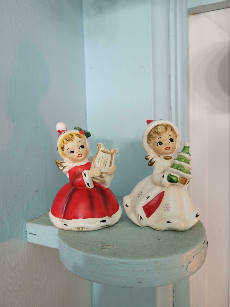 Two nostalgic vintage Christmas decorations featuring girls in holiday dresses holding a lyre and a Christmas tree on a shelf.