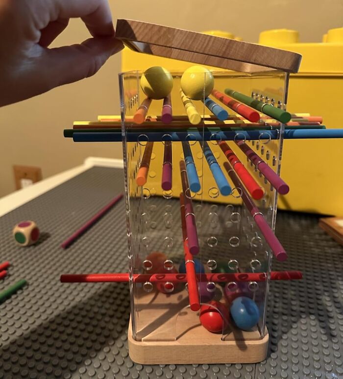 Hand lifting lid of colorful wooden stick game toy, showcasing gifts that unleash 5-year-old joy and playful excitement.