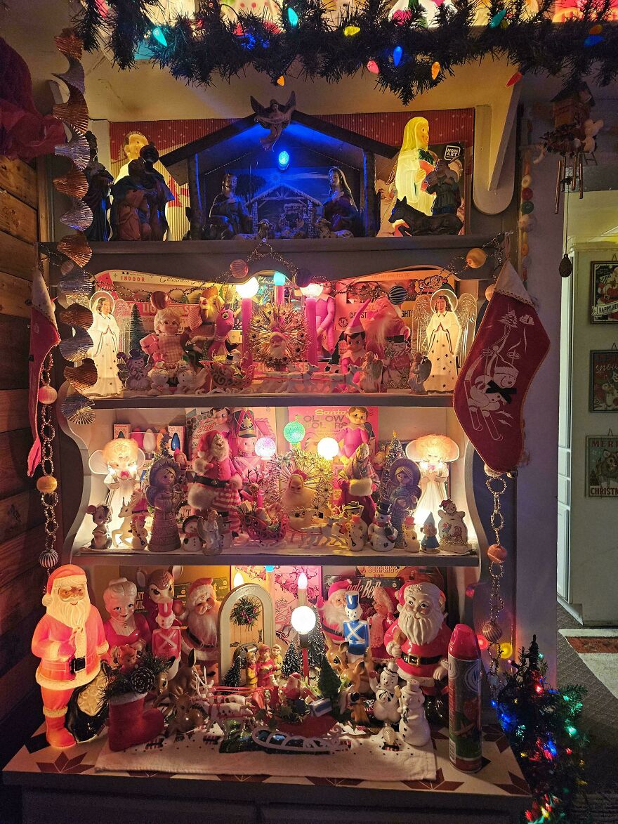 Vintage Christmas decorations display with glowing Santa figures, angels, toys, and colorful string lights creating a nostalgic holiday scene.