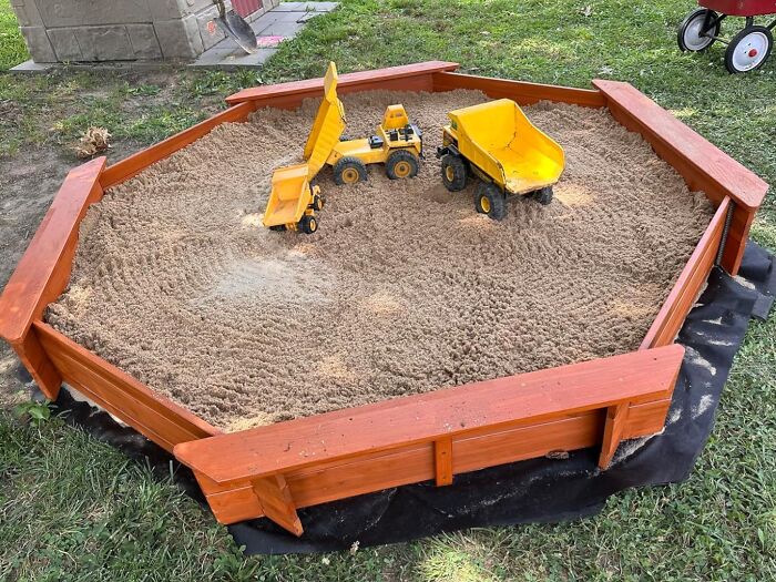 Wooden sandbox with yellow toy dump trucks and construction toys, perfect for gifts that unleash 5-year-old joy.