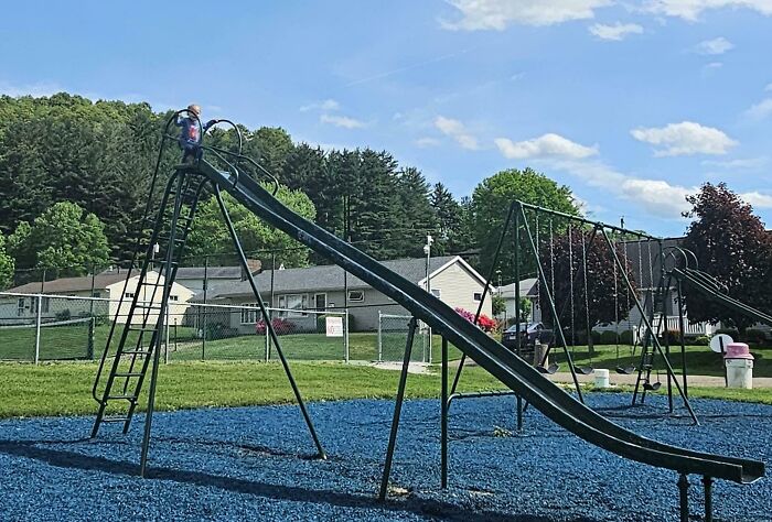 Young child climbing a tall slide at a playground, capturing a wholesome and funny dad moment outdoors.