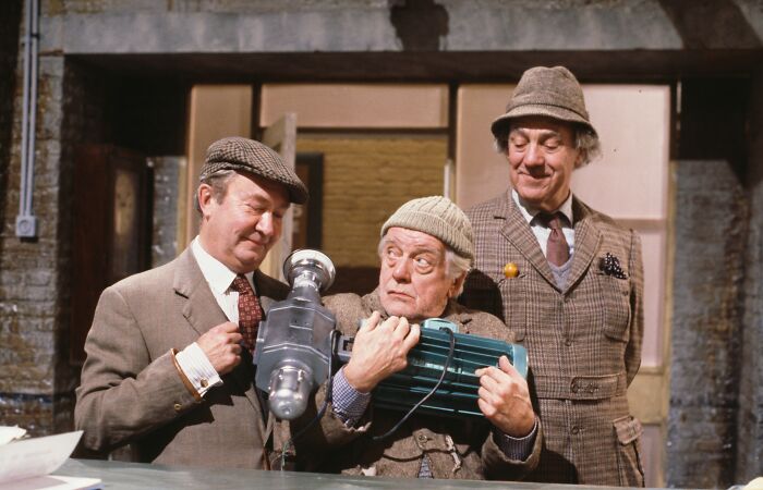 Three men in vintage clothing holding a mechanical object, representing long running TV shows in classic settings.