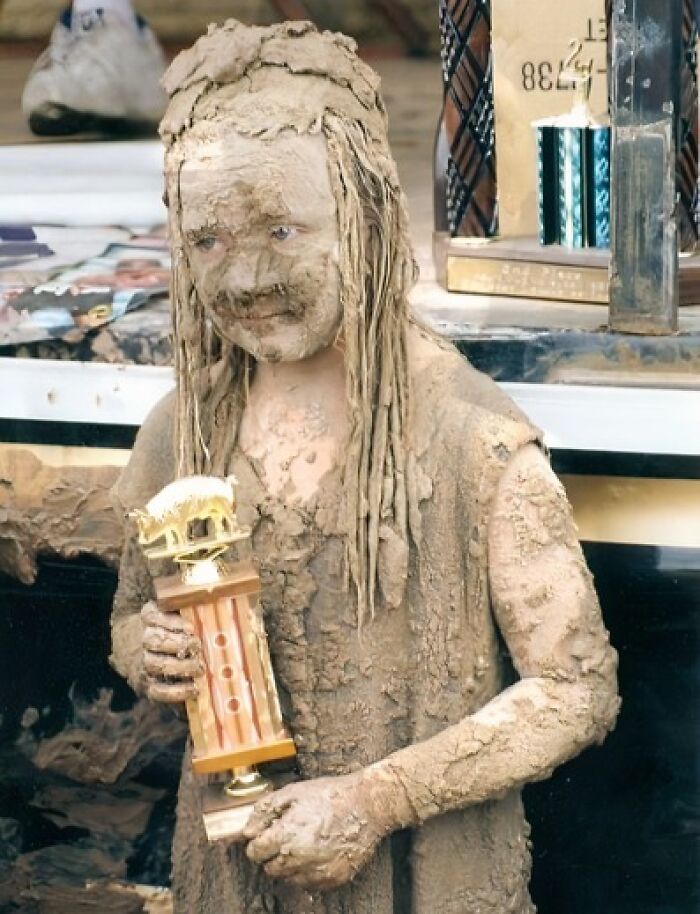 Child covered in mud holding a trophy, capturing a hilariously awkward childhood moment with a muddy face and outfit.