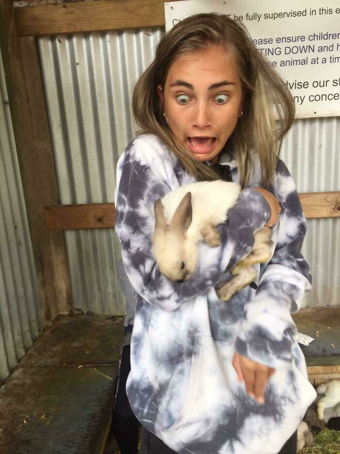 Young woman in a tie-dye hoodie holding a rabbit with a funny and surprised expression, captured at the perfect time.