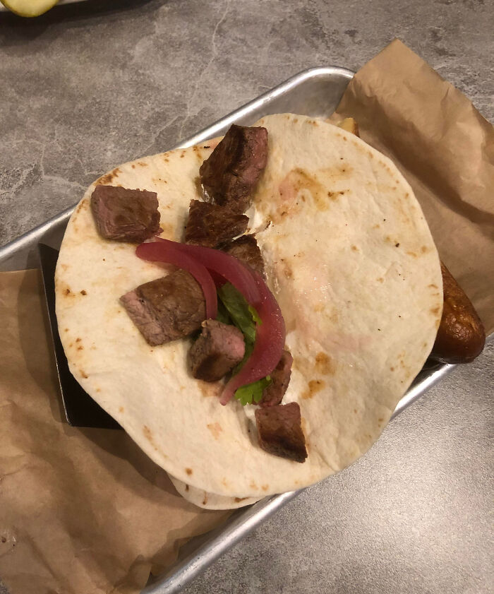 Outrageous meal featuring a small tortilla with a few pieces of steak and pickled onions, far from menu expectations.