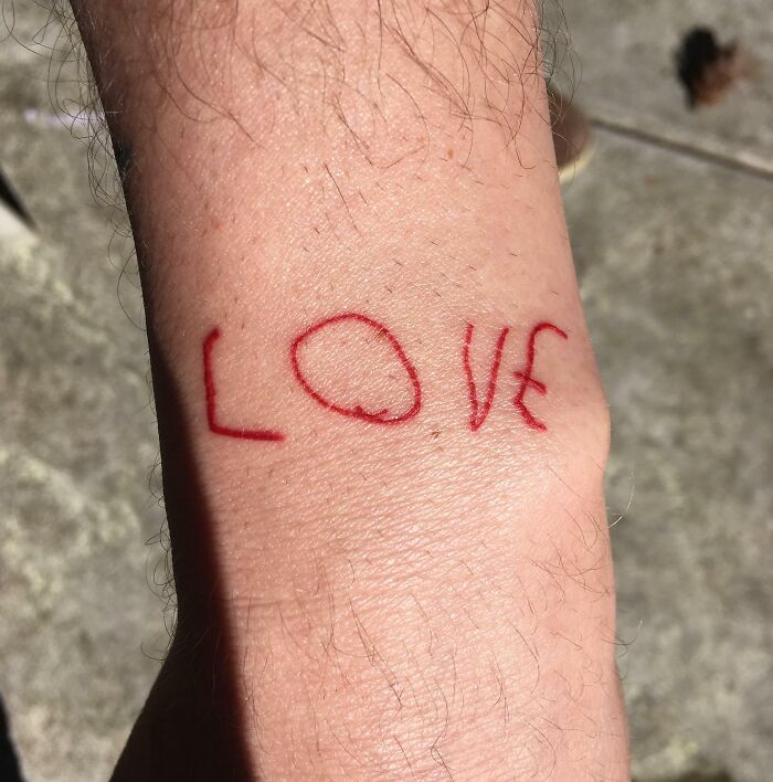 Close-up of a wholesome tattoo on wrist spelling love in red ink, showcasing meaningful small ink design.