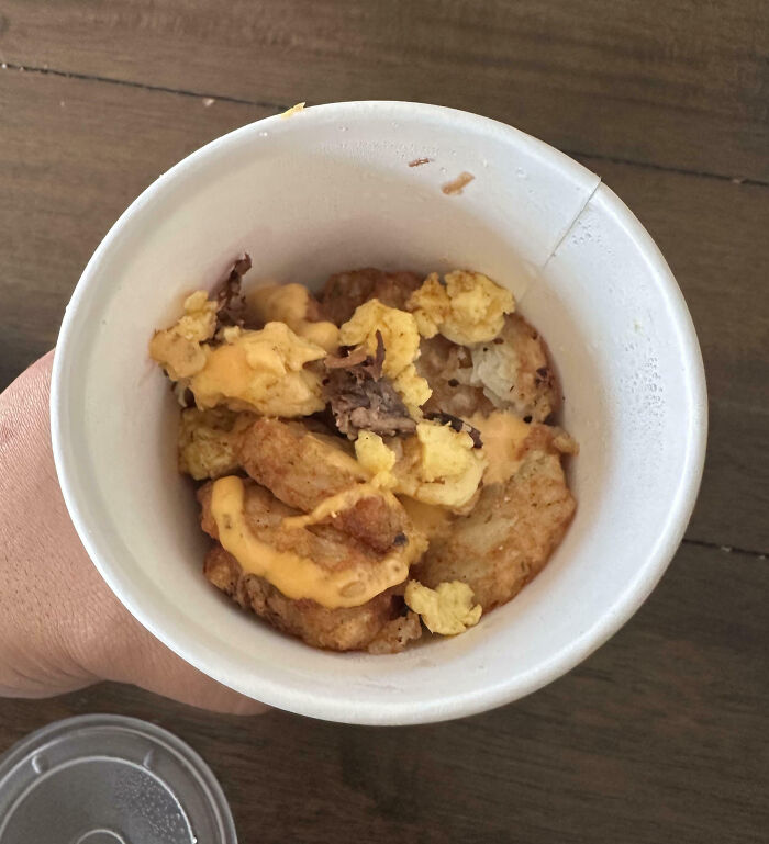 Cup of breakfast with scrambled eggs, tater tots, and cheese sauce, showing an outrageous meal that looks nothing like menu photos.