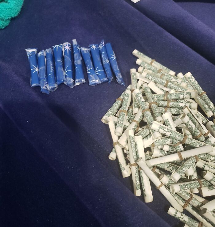 Rolled dollar bills and blue patterned paper rolls arranged on a dark surface as funny gift wraps for Christmas mischief.