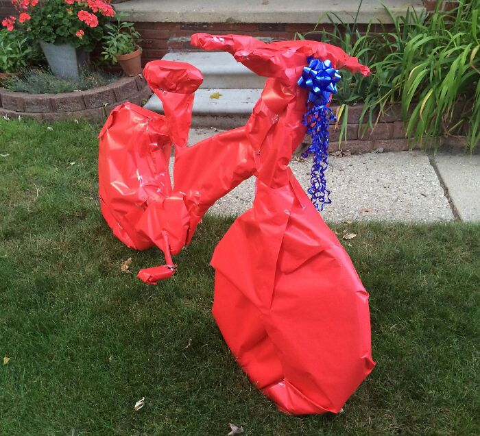 Bicycle wrapped entirely in red gift wrap with a blue bow, showcasing one of the funniest gift wraps for Christmas.