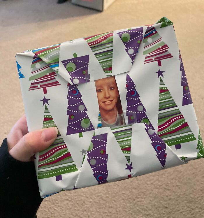 Hand holding a Christmas gift with funny wrapping that reveals a hidden face through the patterned paper.
