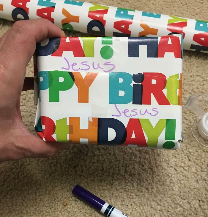 Hand holding a funny gift wrap with colorful happy birthday text and "Jesus" written twice in purple marker.