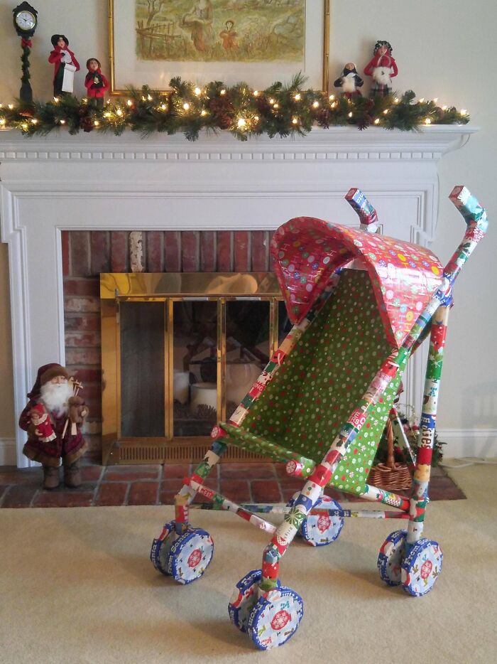 Baby stroller completely covered in colorful funny gift wraps, set in a festive living room with Christmas decorations.