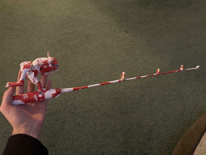 Hand holding a fishing rod creatively made from funny gift wraps with Christmas-themed red and white paper.