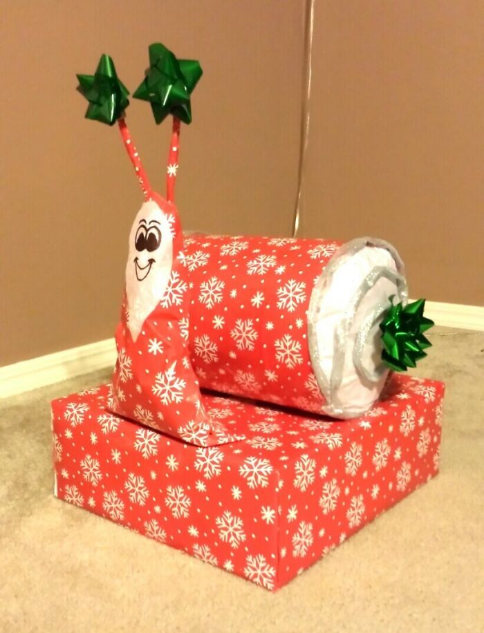 Funny gift wrap shaped like a smiling snail, wrapped in red paper with white snowflakes and green bow decorations.