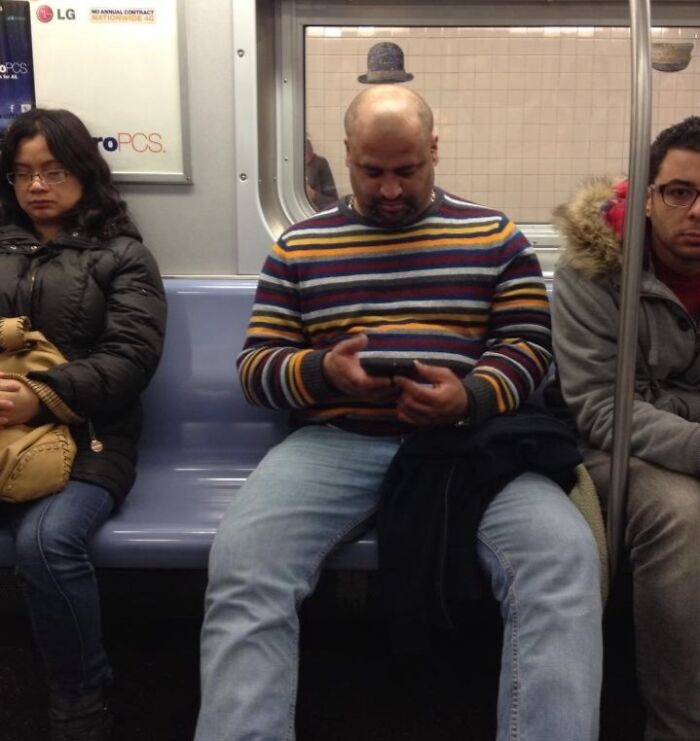 Man sitting on subway with a striped sweater perfectly aligned with a reflection that looks like a hat above his head, funny perfect timing.