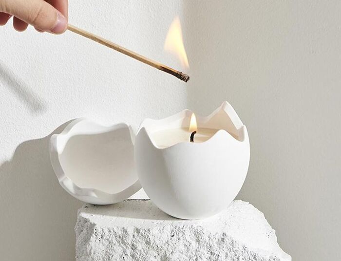 Hand lighting a candle shaped like a c*****d egg, showcasing unique never-before-seen gifts concept.