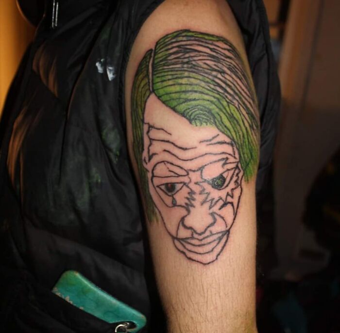 Tattoo of a distorted face with green hair on a person's upper arm, showcasing one of the worst tattoos from an online group.