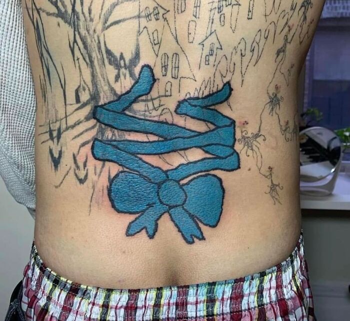 Blue ribbon tattoo with awkward design on lower back, featured in worst tattoos online group that made members cringe.