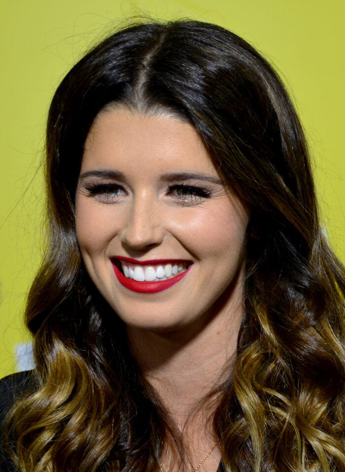 Katherine Schwarzenegger with wavy hair and red lipstick smiling at a public event, highlighting her bio and career.