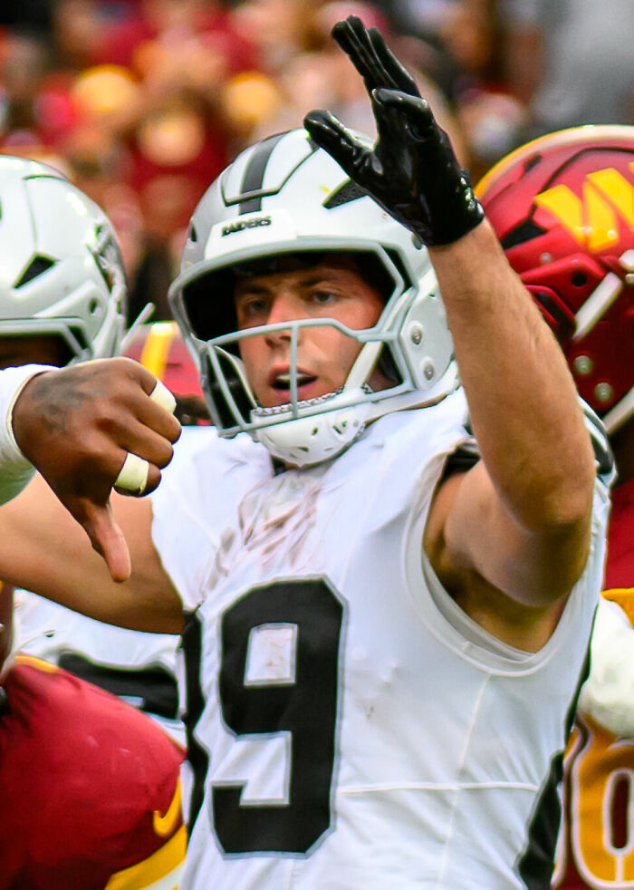 Brock Bowers in white football helmet and jersey celebrating during a game with teammates on the field.